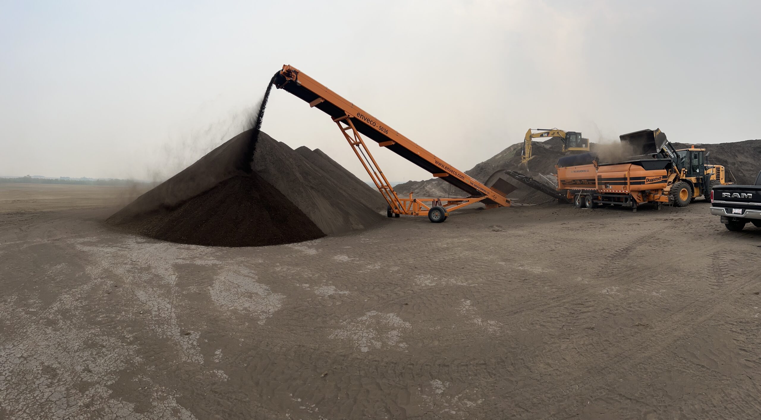 Screened soil and mulch piles being built with a conveyor at the yard