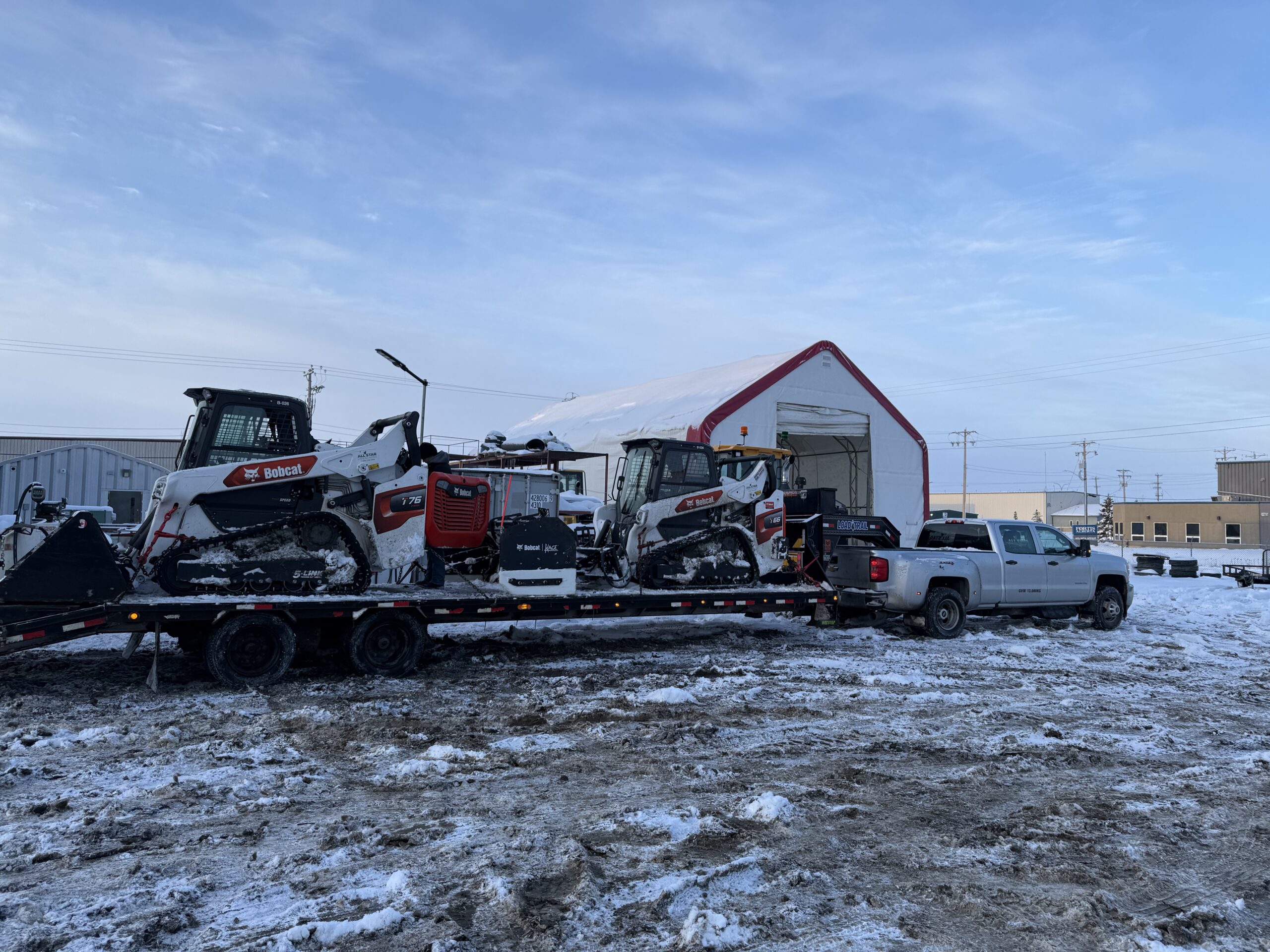 Skid steers loaded on a trailer for a winter snow route
