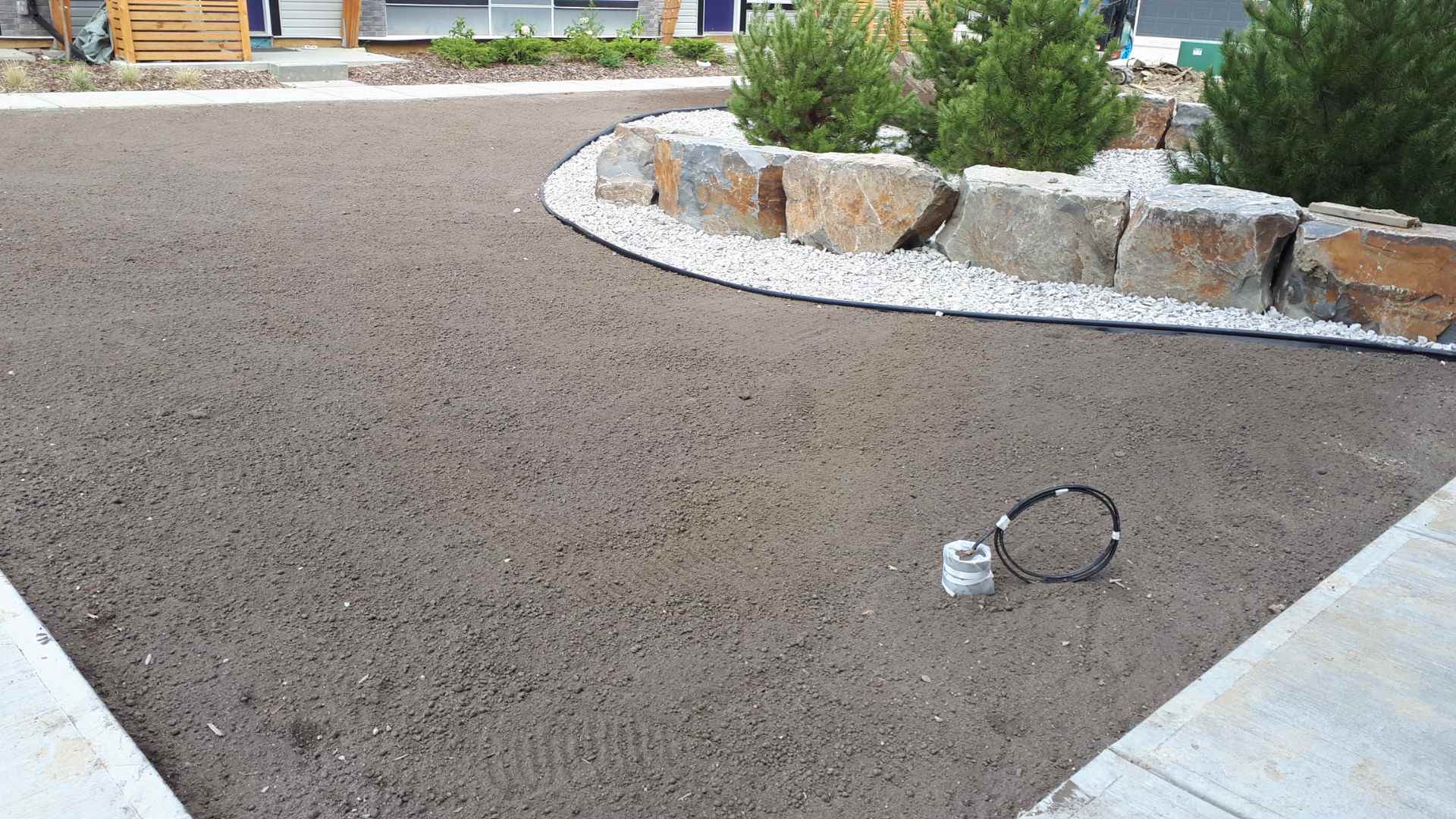 Curved boulder-edged planting bed with white rock and pines
