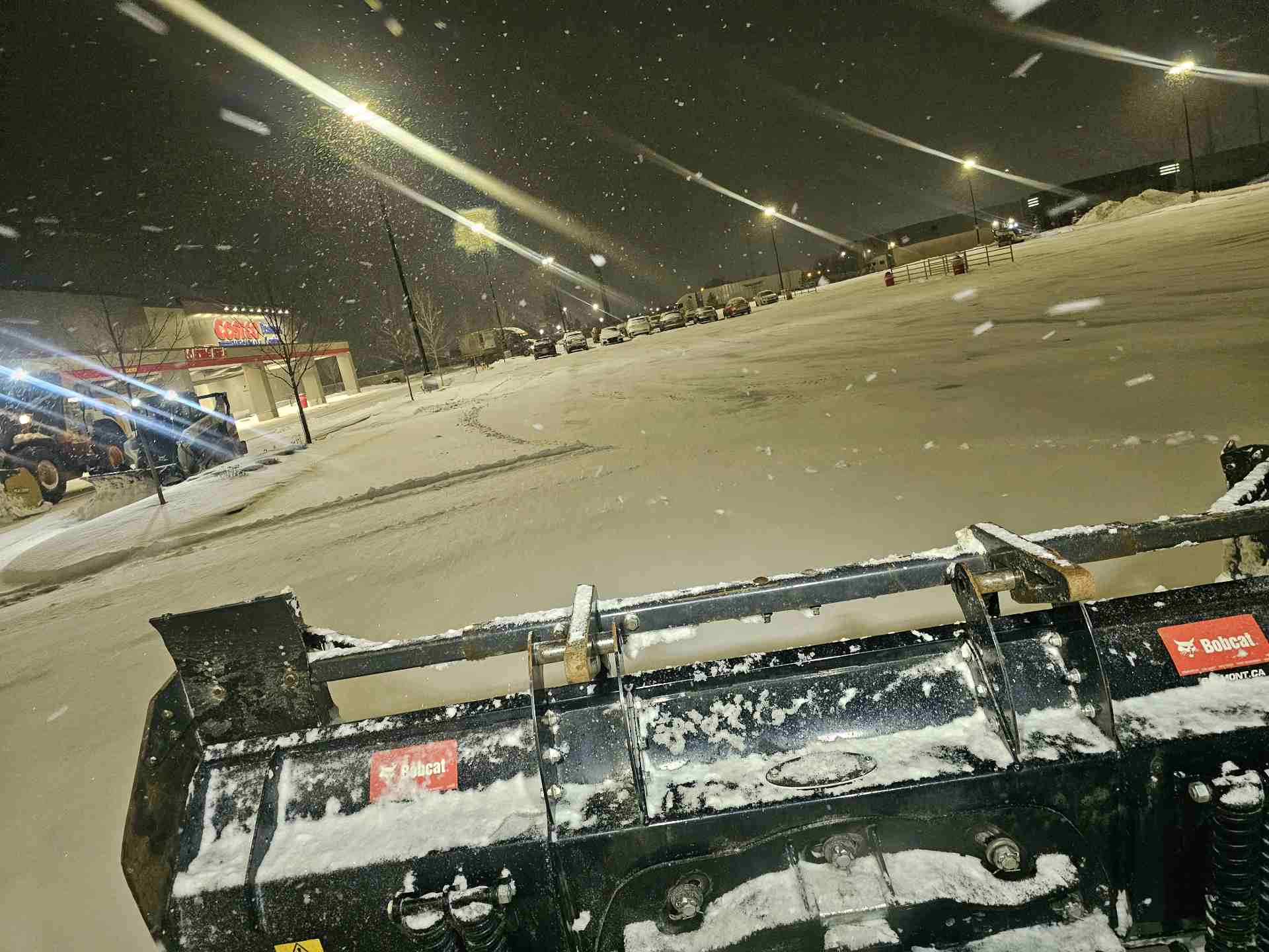 Skid steer plowing a commercial parking lot at night